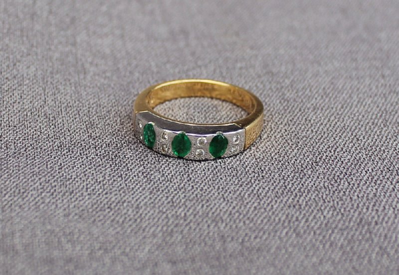 An Emerald and diamond ring set with three oval emeralds and eight brilliant cut diamonds to a