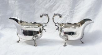 A pair of George V silver sauce boats with a shaped edge, scrolling leaf mounted handle,