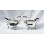 A pair of George V silver sauce boats with a shaped edge, scrolling leaf mounted handle,