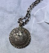 A Paul Arviso white metal pendant of circular form decorated with a log cabin in a landscape