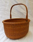 A William and J Reis woven basket of oval form, with a swing handle,