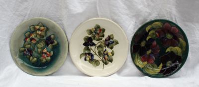 A Moorcroft pottery plate, decorated in the clematis pattern to a dark green ground, 26cm