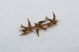 A yellow metal bar brooch in the form of three swallows, set with seed pearls, marked 15c,