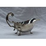 A George V silver sauce boat with a shaped rim, leaf capped scrolling handle and three pad feet,