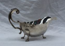 A George V silver sauce boat with a shaped rim, leaf capped scrolling handle and three pad feet,