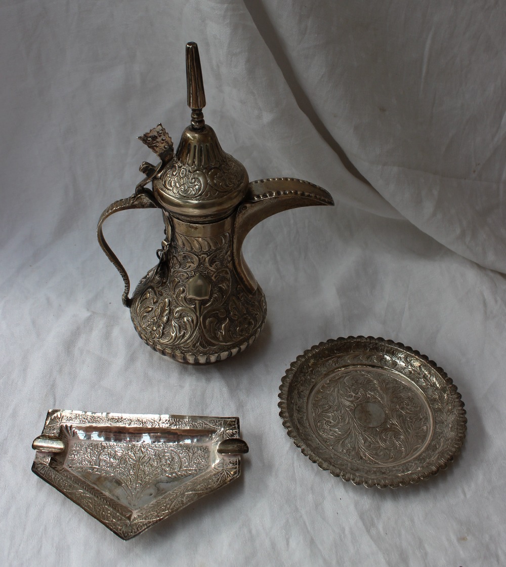 A white metal teapot, with a domed pointed lid, the body embossed with leaves and flowers,