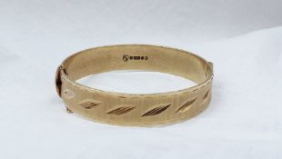 A 9ct yellow gold hinged bangle, with line and leaf decoration,