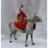 A Beswick model of a guardsman, seated on a grey horse, with a red plume, red coat and holding a