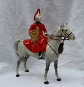 A Beswick model of a guardsman, seated on a grey horse, with a red plume, red coat and holding a