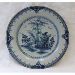 A 19th century tin glazed earthenware plate decorated with trees, flowers and a fence pattern in