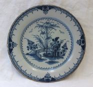A 19th century tin glazed earthenware plate decorated with trees, flowers and a fence pattern in