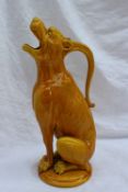 A Burmantoft Art Pottery faience grotesque jug in a mustard yellow glaze, in the form of a seated