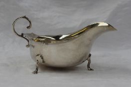 A George V silver sauce boat with a flared rim, with a C scroll handle on three legs, Chester, 1914,