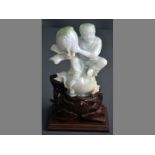 A MODERN CHINESE GREEN AND WHITE HARDSTONE CARVING of a boy seated on a peach, holding a peach of