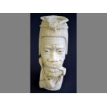 AN AFRICAN CARVED IVORY HEAD of an elder smoking a pipe and holding an axe, wearing a traditional