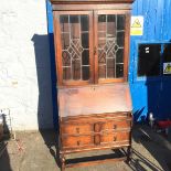 An oak bookcase bureau with leaded glass doors and two drawers below the desk.