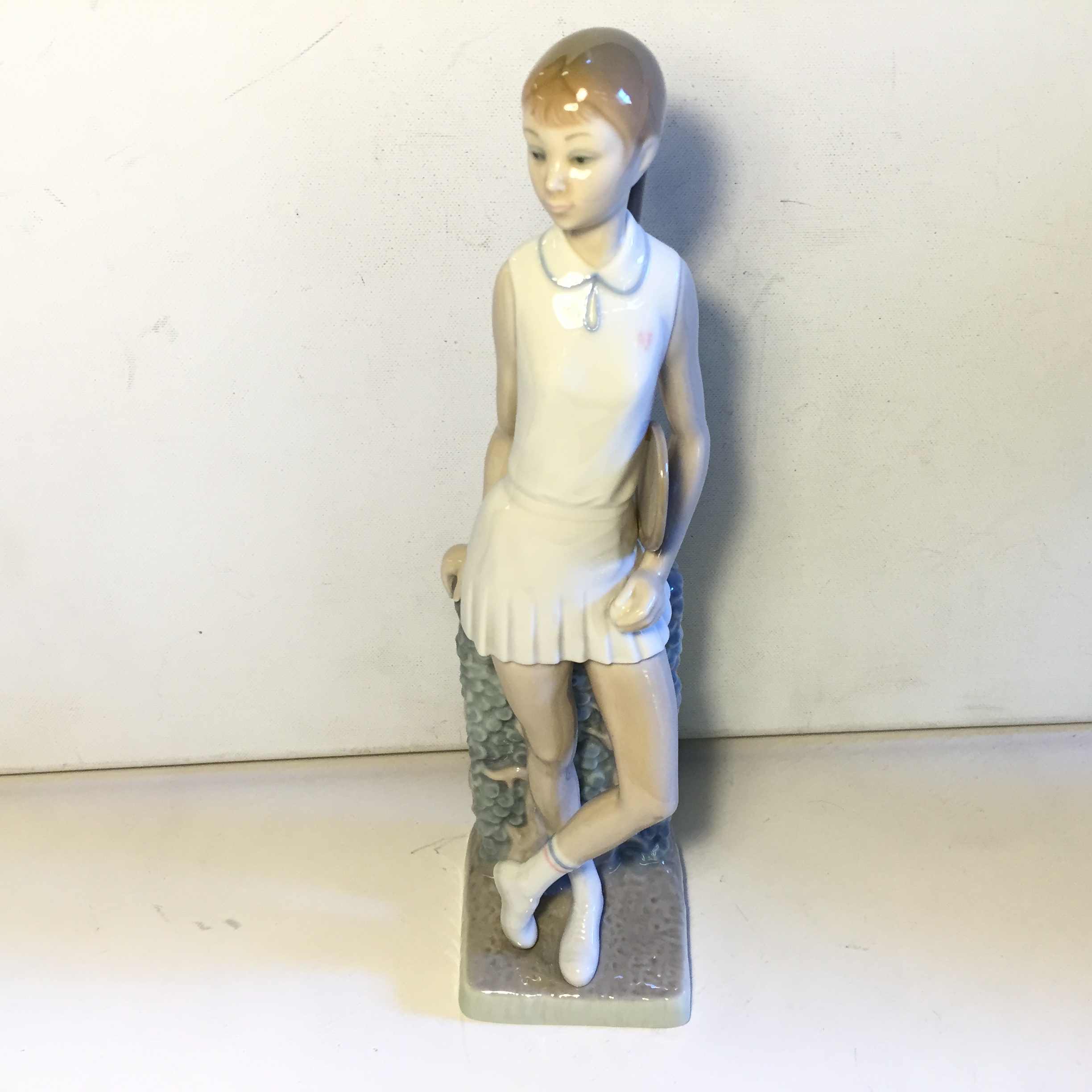A Lladro figurine of a girl playing in a tennis outfit.