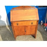 An oak bureau with single drawer above shelved cupboard.