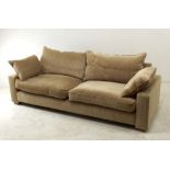 A modern four seater sofa with loose cushions to back and sides, upholstered in beige velour