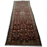 A hand knotted Kazak runner with red ground and geometric repeating design, 304 by 106cm.