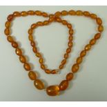 A string of fifty six early 20th century amber beads, polished and cut, of graduated form,