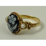 A Victorian mourning ring the central black onyx cameo cut with a flower, flanked by seed pearls