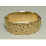 An 9ct gold plated bangle, engraved with floral and foliate decoration, with a metal core.