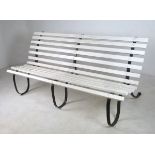 A white painted wooden slatted garden bench on three cast iron scroll supports,