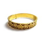 An Oriental gold circular bangle, decorated with character motifs, alternating with flowerheads,