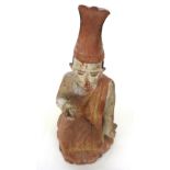 A South East Asian polychrome decorated carved wood figure depicting a robed monk seated atop a