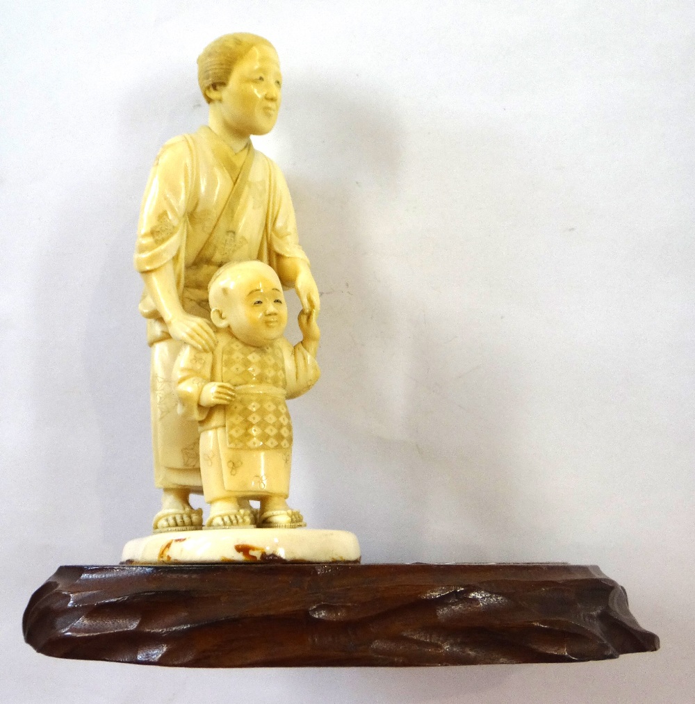 A Japanese ivory okimono of a woman helping a child to walk, Meiji period,