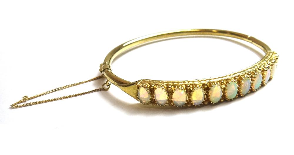 A gold and opal set oval hinged bangle, the front mounted with a row of eleven oval opals,