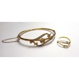 A gold and seed pearl set oval hinged bangle, the front with a central flowerhead motif,