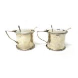 A pair of silver mustard pots, each of cylindrical form, decorated with a gadrooned rim,