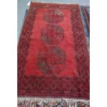 An Afghan rug, the plain madder field with three bold guls, a diamond border, 180cm x 105cm.