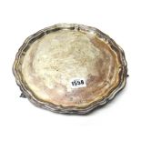 A silver salver, of shaped circular form, with a pie-crust rim, raised on three scrolling feet,