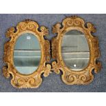 A pair of 19th century North Italian carved softwood mirrors with shaped oval frames,