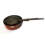 A graduated matched set of three Victorian copper shallow pans, each with a wrought iron handle,