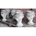 A set of six reconstituted stone garden urns with relief moulded floral bodies and moulded socles,