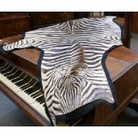 Taxidermy; a zebra skin rug with black linen backing, 260cm.