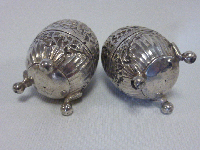 A pair of Continental white metal pepperettes of ovoid form raised on three ball feet with stylised - Image 2 of 2