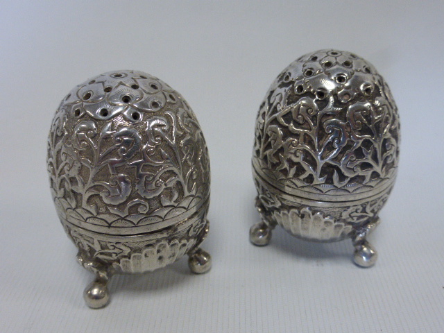 A pair of Continental white metal pepperettes of ovoid form raised on three ball feet with stylised