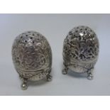 A pair of Continental white metal pepperettes of ovoid form raised on three ball feet with stylised