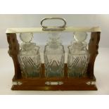 AN EDWARDIAN OAK AND SILVER PLATED FRAMED TANTALUS containing three cut glass spirit decanters