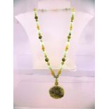 A NEPHRITE NECKLACE OF SPHERICAL BEADS, sampler colours, and carved pendant, 106g, 68cm long