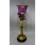 A VICTORIAN OIL LAMP, having brass stem on ebonised base, glass reservoir with pink tinted glass