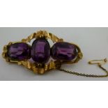 A GOLD COLOURED METAL MOUNTED THREE STONE AMETHYST SCARF BROOCH having three mixed cut stones in a