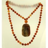 AN ORIENTAL JADE CARVED PENDANT decorated with fish on a row of carnelian beads, 90cm long