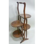 AN EDWARDIAN MAHOGANY FOLDING CAKE STAND with four dished tiers, 77cm high