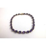 A GOLD COLOURED METAL LINK BRACELET, having twenty-three oval claw set amethysts around, 18cm long